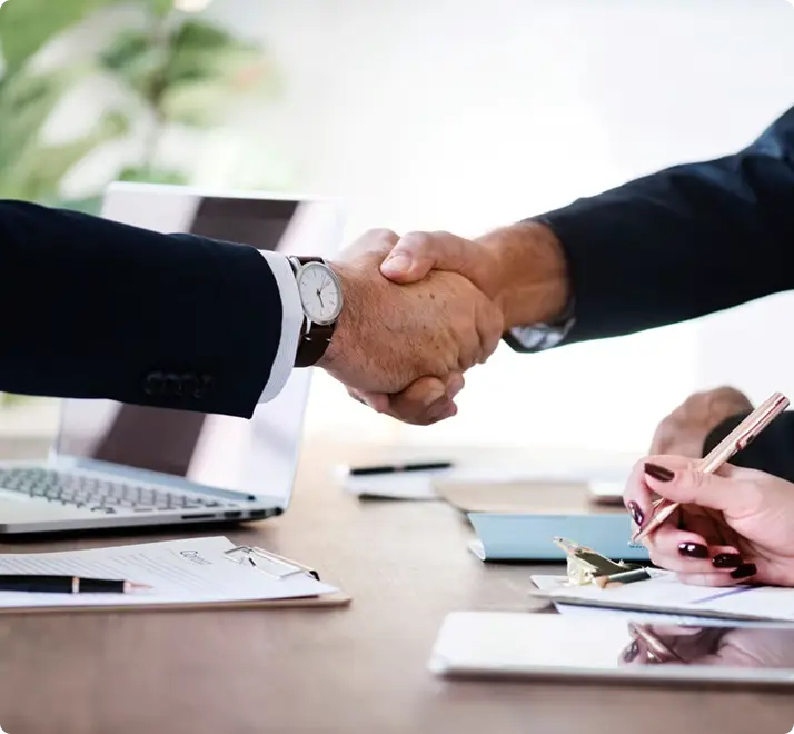 Two colleagues shaking hands over a laptop