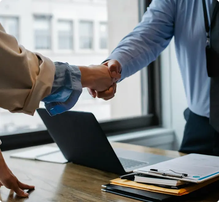 Two individuals shaking hands over a laptop